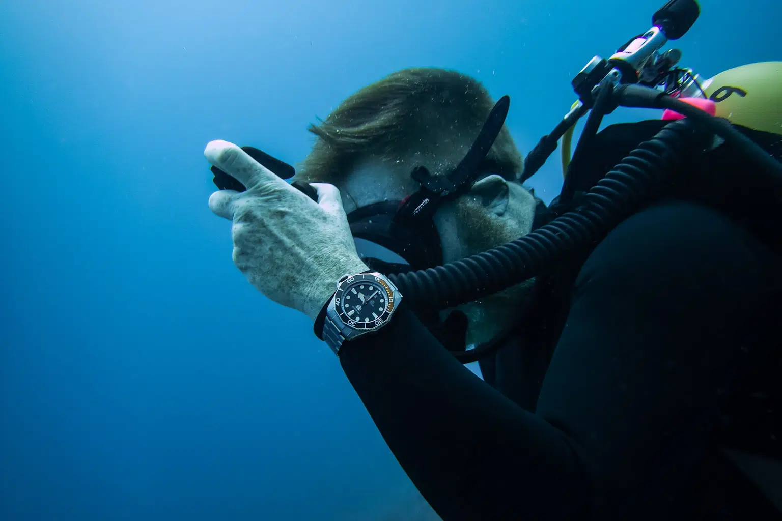 A scuba diver underwater wearing a dive watch with a rotating bezel, demonstrating practical use in diving