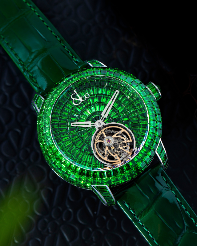 Luxury green gemstone tourbillon watch with emerald baguette-cut dial and skeletonized movement on alligator strap